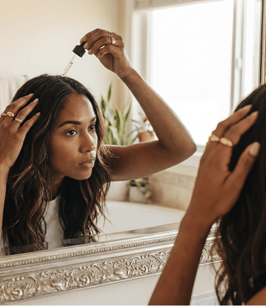 A woman applying The Scalp Serum at her mirror